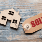 Paper house cutout with a tag labeled SOLD on a wooden surface