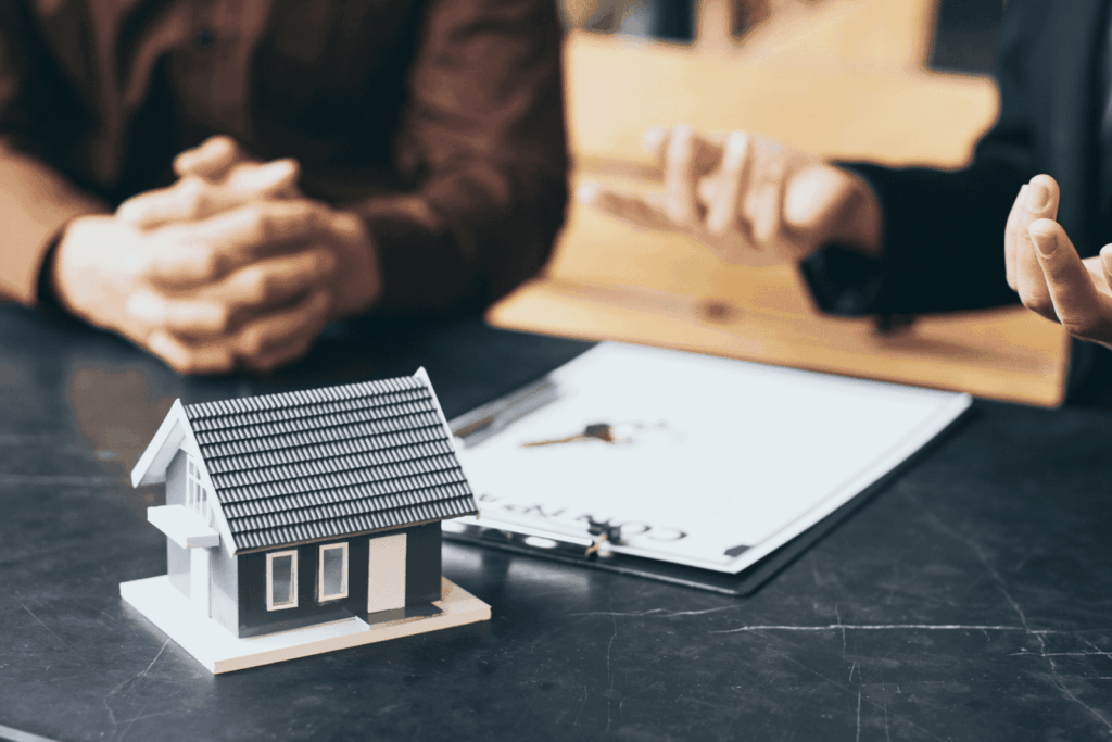 People discussing a property deal with a small house model and contract on the table.
