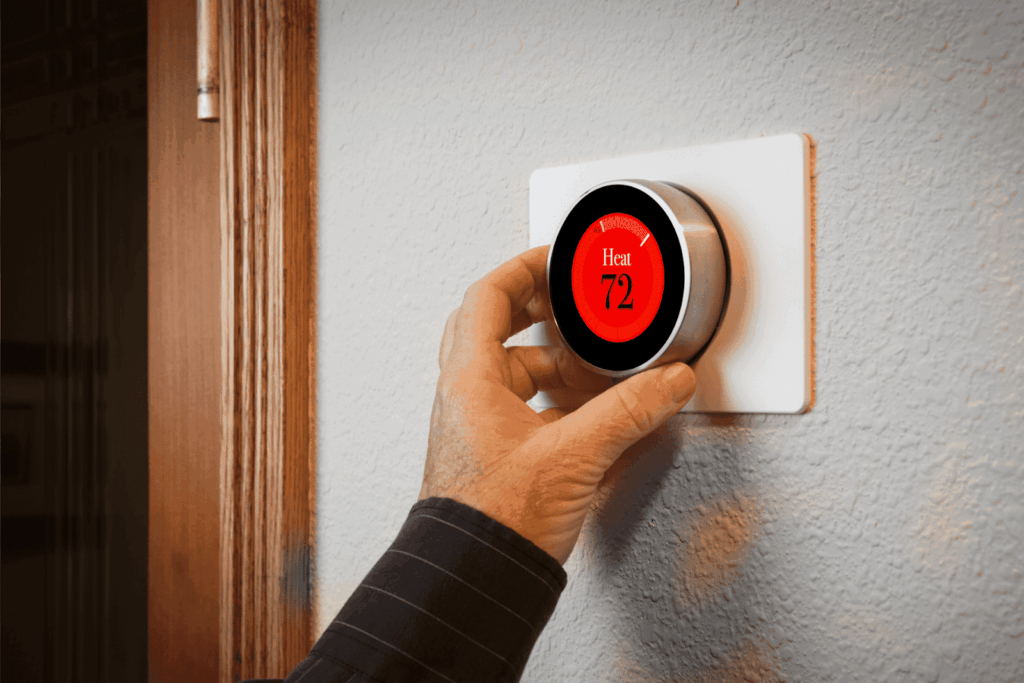 Person adjusting a smart thermostat set to 72 degrees for heating.