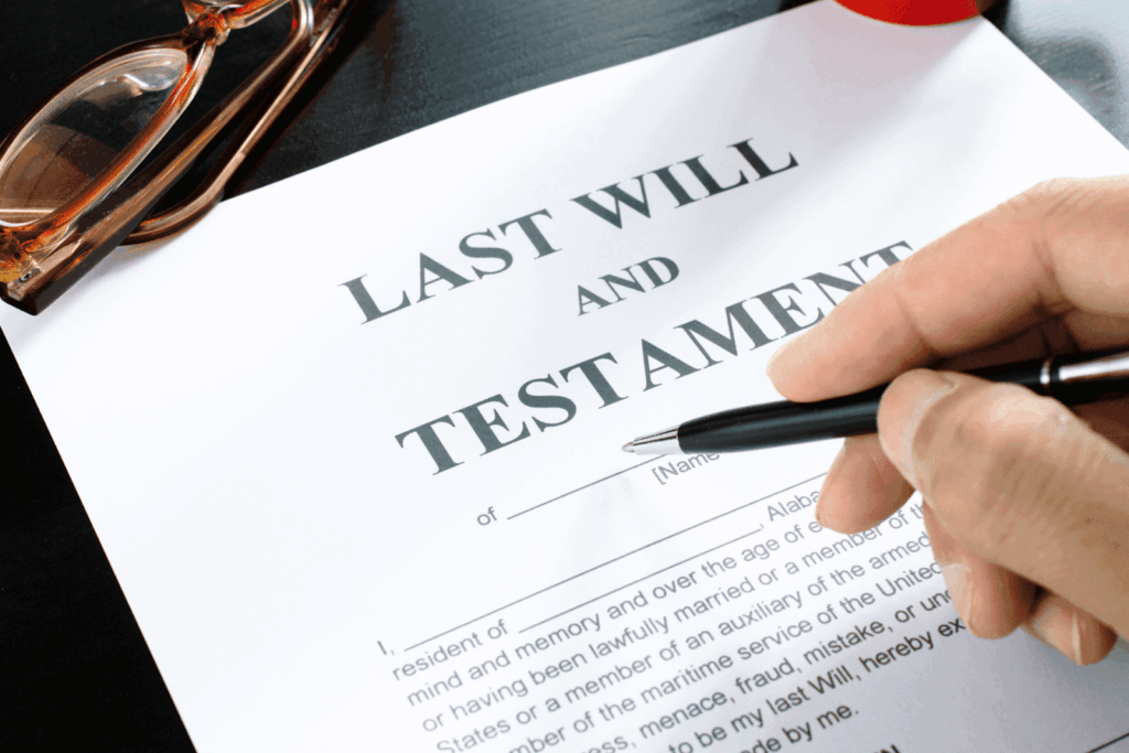 Person holding a pen over a last will and testament document on a desk.