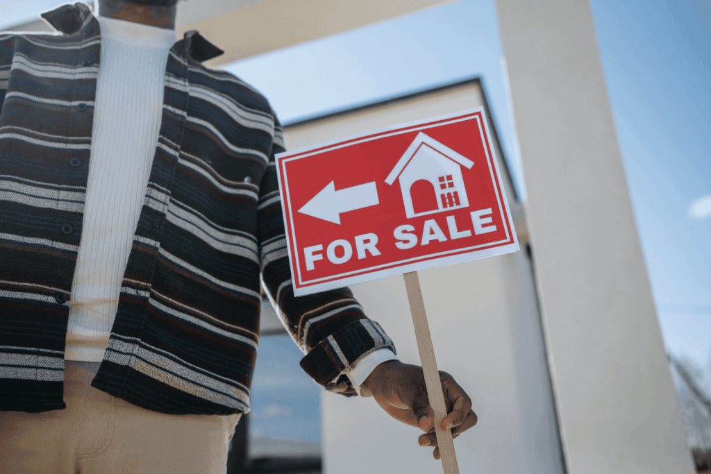 Person holding a red For Sale sign in front of a house
