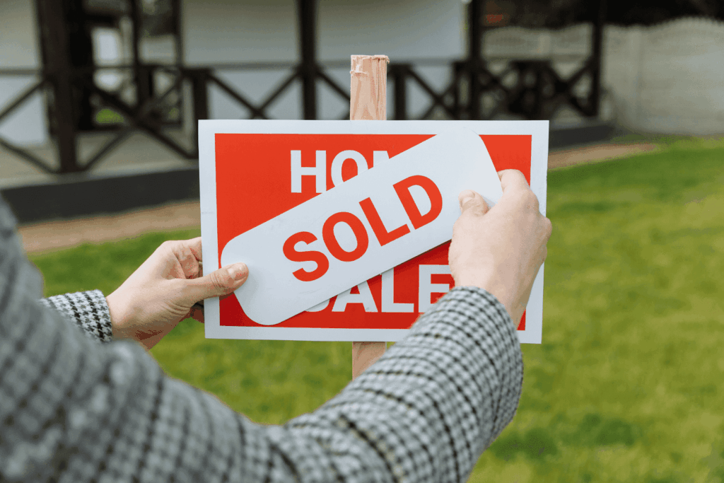 Person placing a “SOLD” sticker on a red “Home for Sale” sign in front of a house.