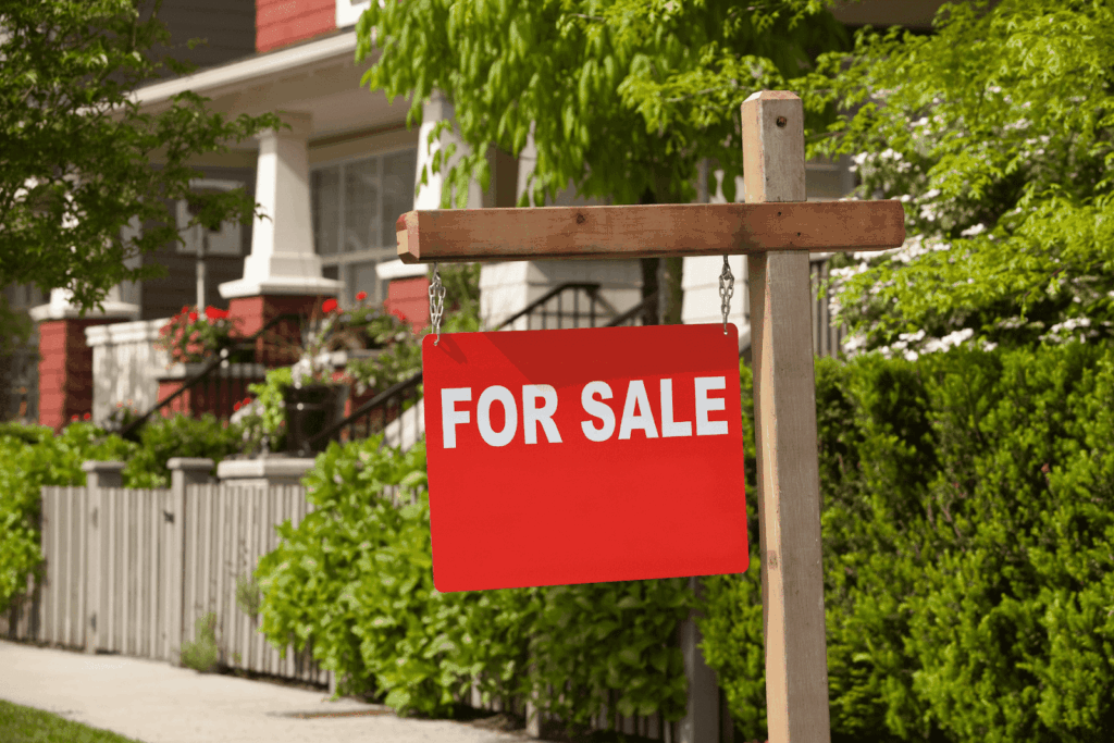 Red For Sale sign in front of a house with green landscaping