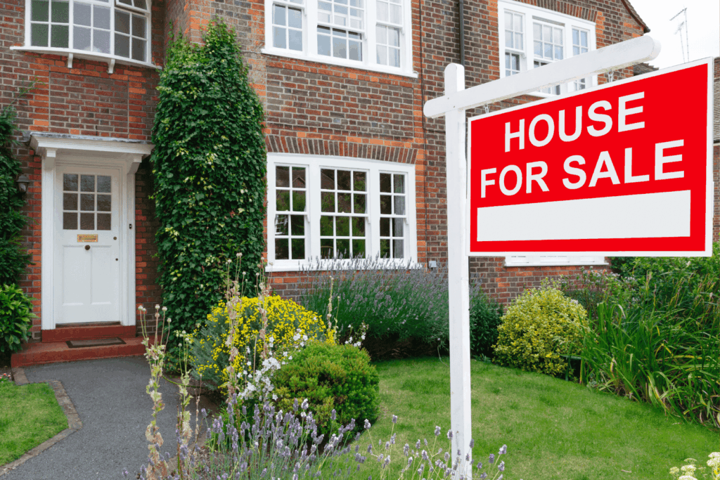 Red and white ‘House For Sale’ sign outside a brick house with a garden