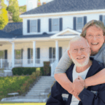 Smiling senior couple hugging in front of their house.