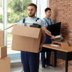 Two movers carrying boxes and equipment in a modern room.
