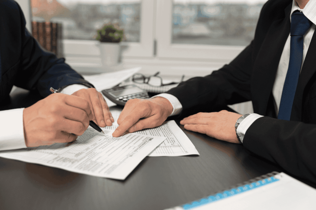 Two people in suits reviewing and signing documents at a desk