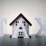 Wooden house between large white letters spelling TAX