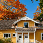 Yellow house with autumn trees and blue sky in the background.
