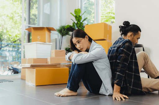 A Sad couple sitting back-to-back on the floor among moving boxes, looking upset as they go through a divorce