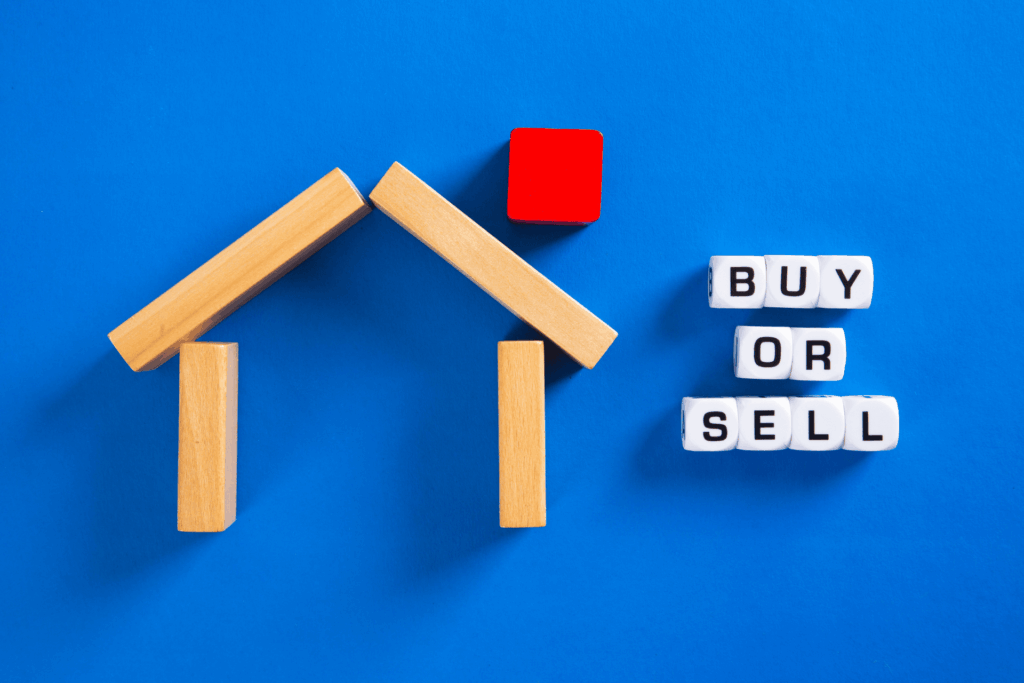 Buy or sell concept using wooden house blocks on blue surface.