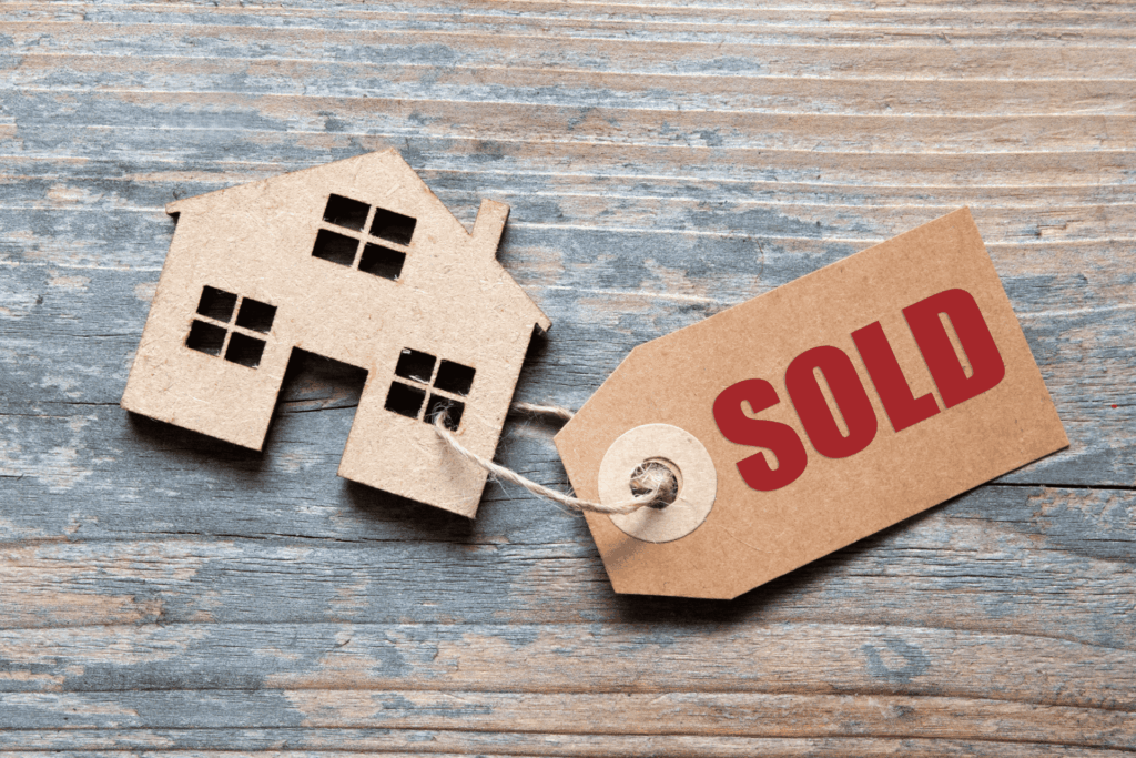 Cardboard house cutout with sold tag on wooden background.