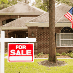 Home for sale with red sign and American flag in the yard.
