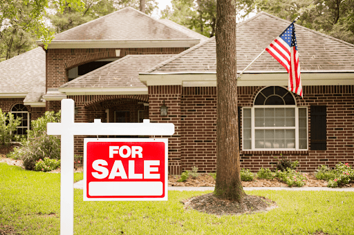 Home for sale with red sign and American flag in the yard.
