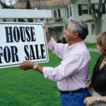 Homeowners putting up a house for sale sign on their property.