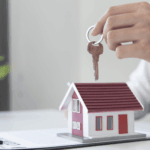 Keys held over model house symbolizing new home ownership.