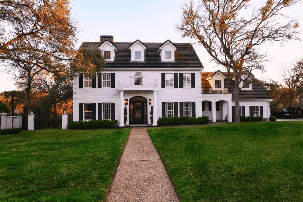Large two-story white brick house with black shutters and spacious front lawn.