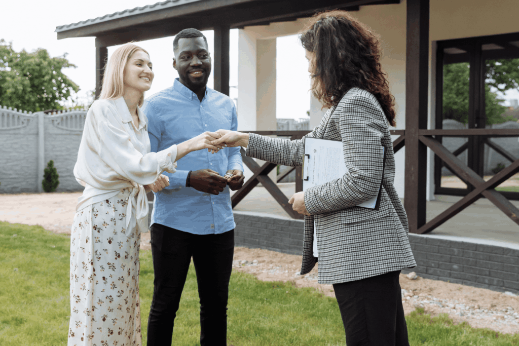 Real estate agent handing keys to a smiling couple outside their new home.