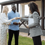 Real estate agent handing keys to a smiling couple outside their new home.