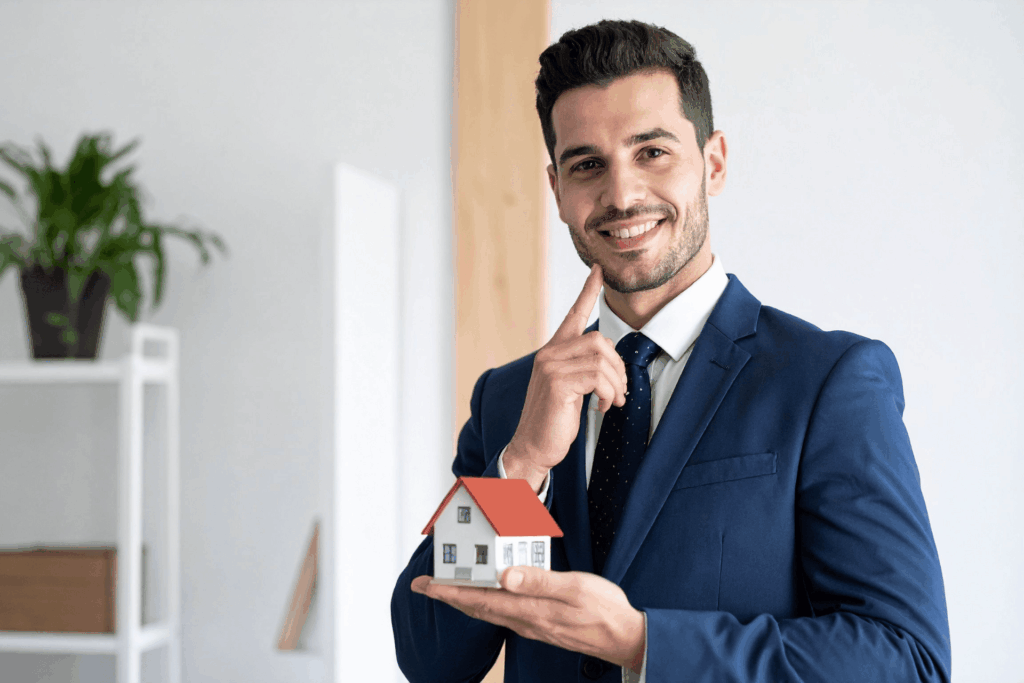 Smiling real estate agent in a blue suit holding a small model house.