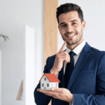 Smiling real estate agent in a blue suit holding a small model house.