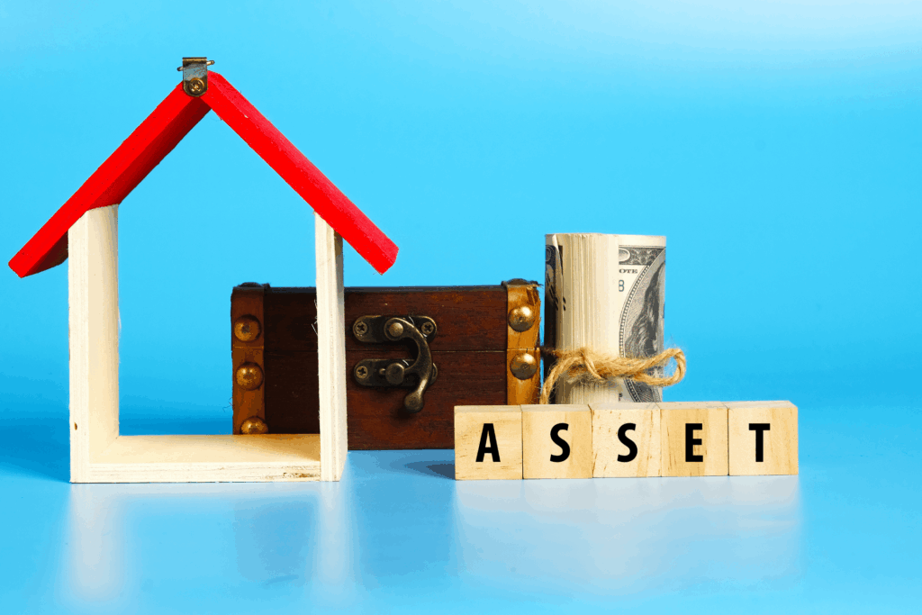 Wooden house frame, cash, and blocks spelling “ASSET,” symbolizing assets divided.