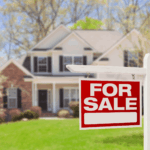 Red and white “For Sale” sign in front of a suburban house.