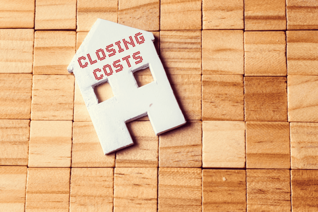 Wooden house cutout labeled “Closing Costs” placed on a wood block background.