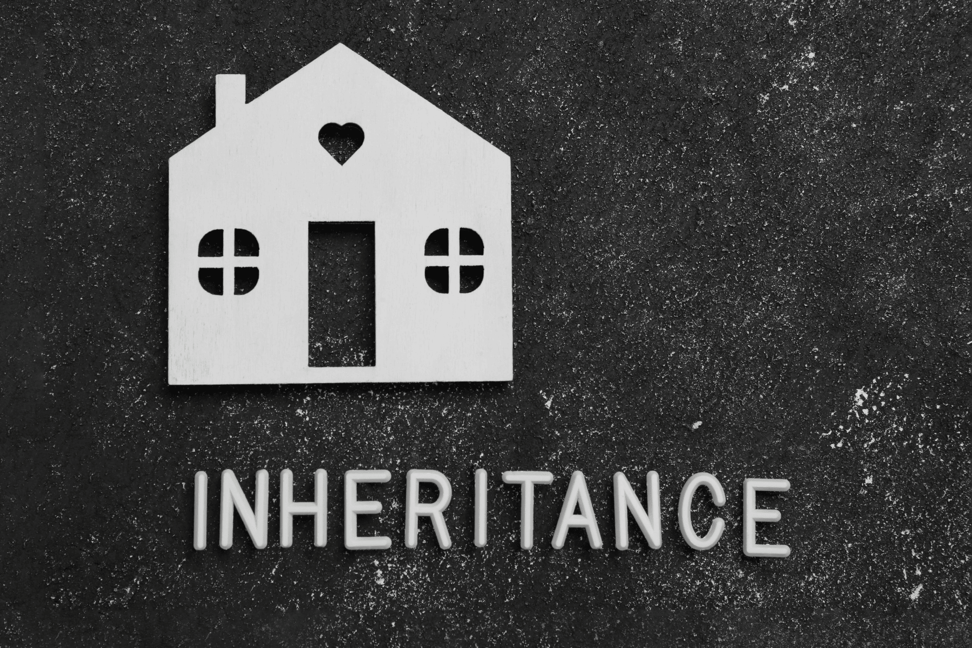Wooden house cutout above the word “INHERITANCE” on a dark textured background.