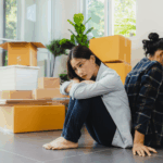 A Sad couple sitting back-to-back on the floor among moving boxes, looking upset as they go through a divorce