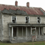 Old abandoned house with broken windows, peeling paint, and a damaged roof.