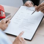Two people reviewing a contract with a house model on the table, illustrating issues that can arise when a property is not in a trust.