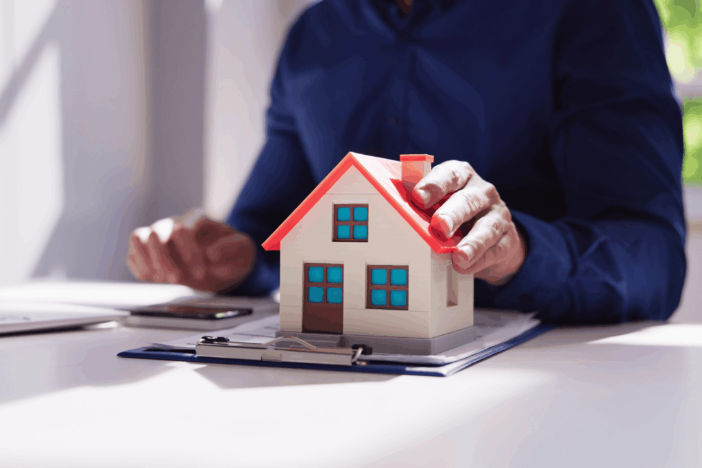 Person holding a small house model on paperwork, symbolizing estate tax considerations when selling a house.