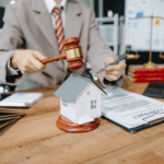Lawyer holding a gavel beside a small house model and contract documents, symbolizing legal decisions about property.
