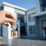 Hand holding house-shaped keychain with key in front of modern house