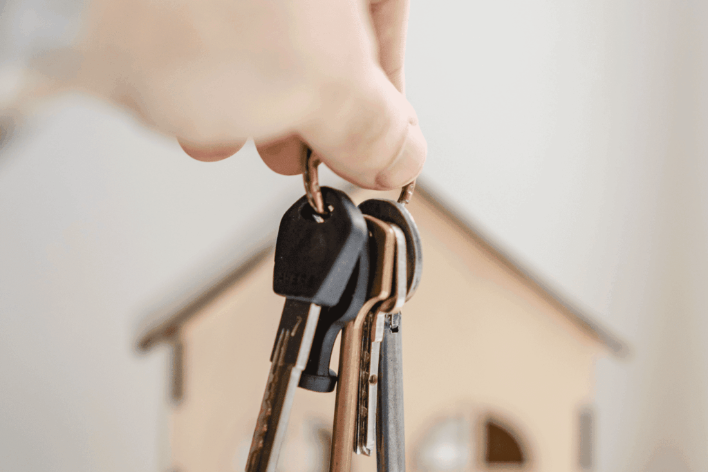 Hand holding house keys with small wooden house in background