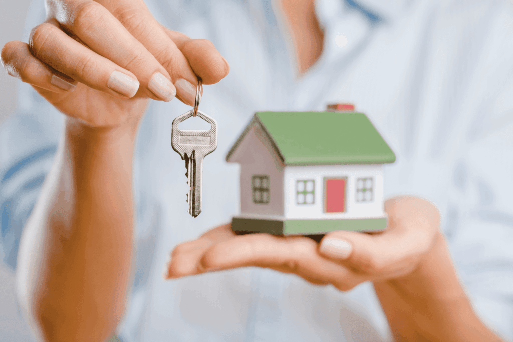 Person holding a key and a small house model.