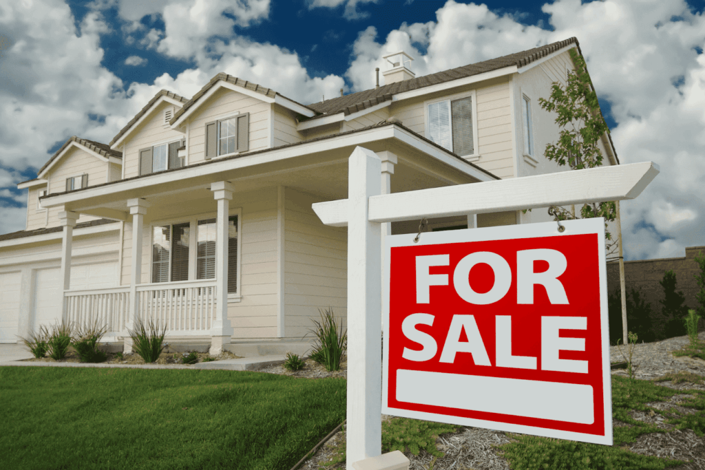 Red “For Sale” sign in front of a suburban two-story house with a lawn.