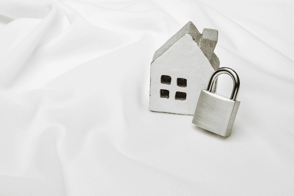 Small house figurine next to a padlock on a white surface, symbolizing home security