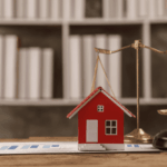 Small model house with legal scales and a gavel on a desk symbolizing real estate law.