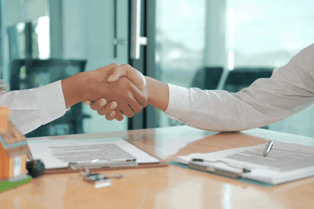 Two people shaking hands over real estate documents on a desk