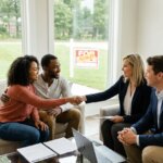A smiling couple shaking hands with a woman in a suit, with a For Sale - Sold sign visible outside.