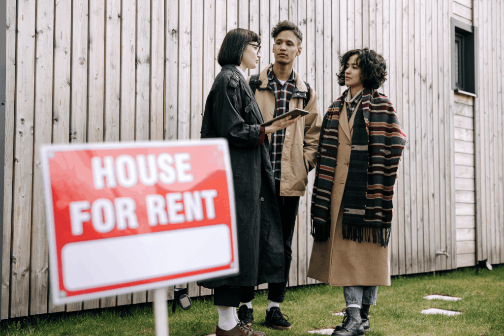 Landlord speaking with prospective tenants next to a house for rent sign outside a residential property in Arkansas.