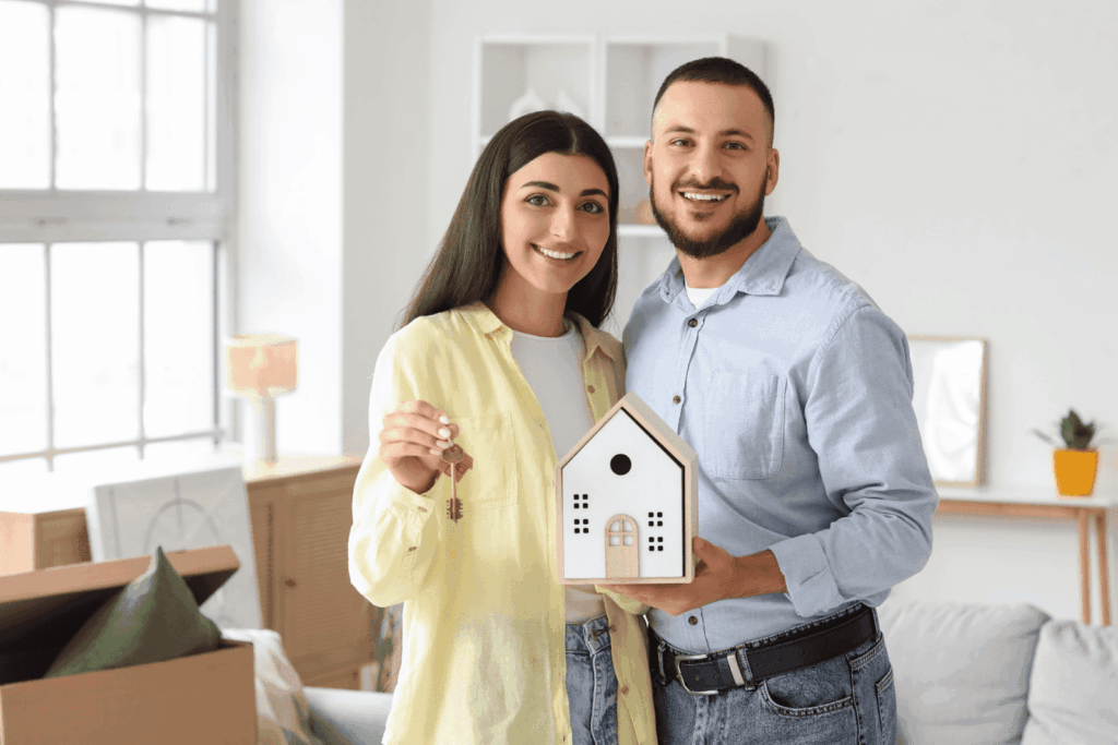 A smiling couple holding house keys and a small house model in their new home.