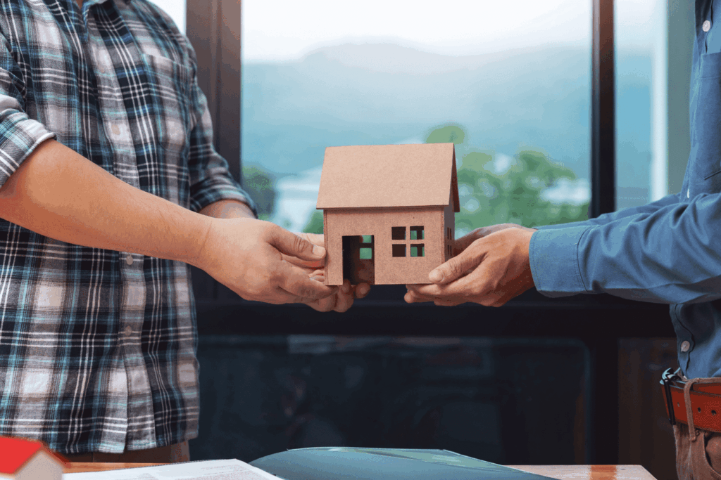 Two people exchanging a small house model, symbolizing a property transfer or real estate deal.