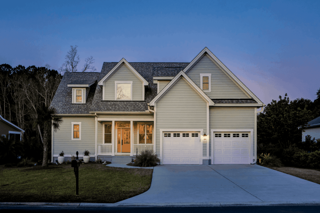 Two-story suburban house with a front porch, lit windows, and a double garage at dusk.
