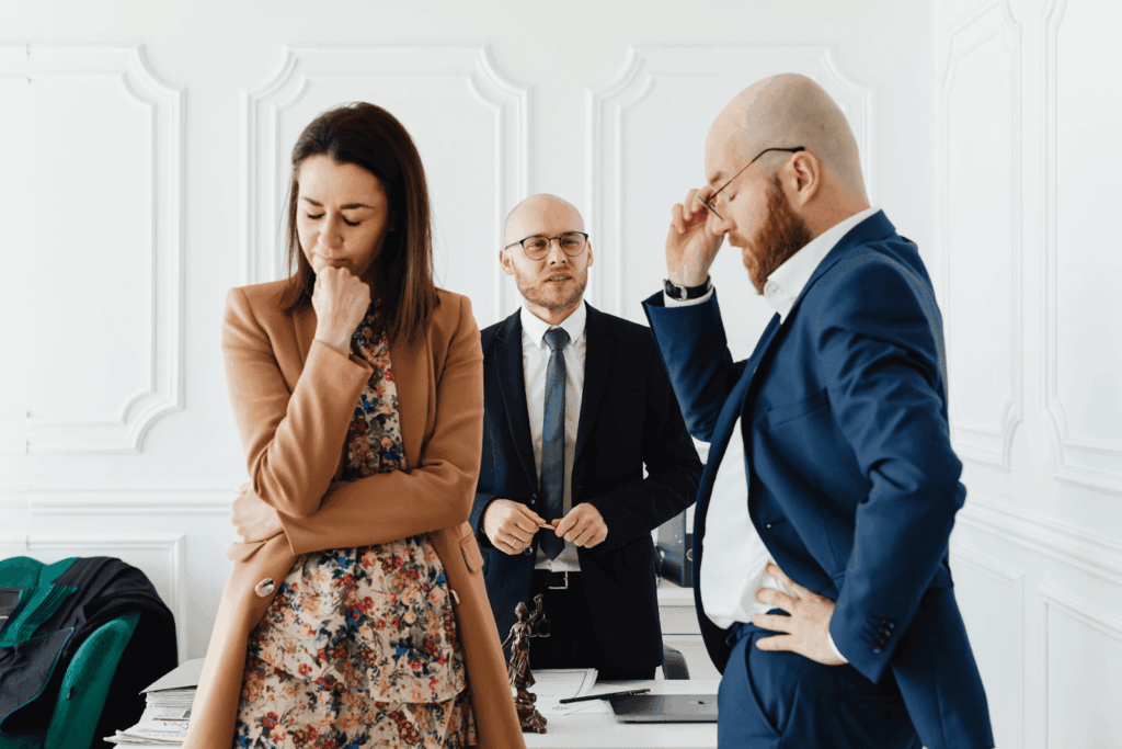 Upset couple standing with a lawyer in an office, suggesting a divorce or legal dispute meeting.