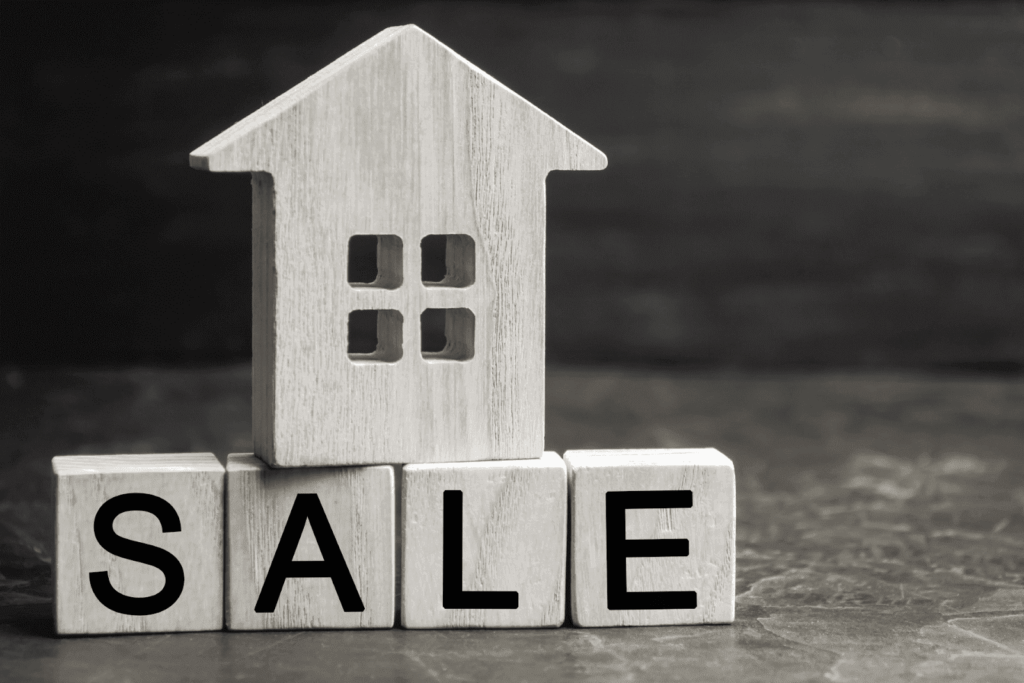 Wooden house model placed on blocks spelling “SALE,” symbolizing a home sale or real estate listing.