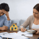 A divorcing couple reviews paperwork at a table with a small model house and cash, symbolizing negotiating a property buyout during divorce.