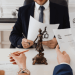Divorce attorneys reviewing and signing divorce decree documents across a desk with a Lady Justice statue during a legal meeting.